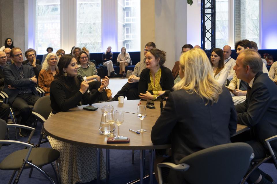 Drie Kamerleden aan een tafel in het midden van een zaal waarin mensen toekijken. PvdA-Kamerlid Songül Mutluer heeft de microfoon en vertelt over haar ervaringen aan tafel met de Kamerleden Kees van der Staaij (ChristenUnie) en Queeny Rajkowski (VVD). 