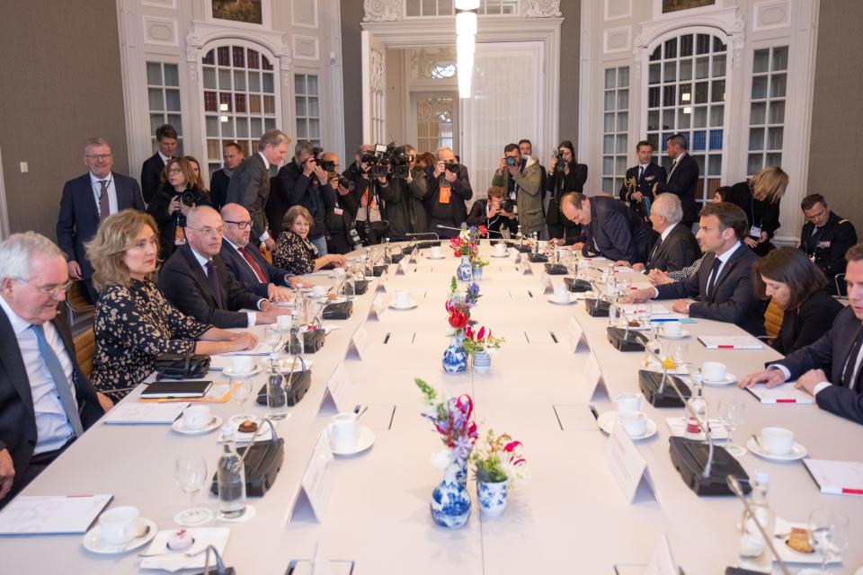 Een lange ovalen tafel met links de Nederlandse Voorzitters en de waarnemend Griffier, rechts president Macron en zijn staf. Aan het einde van de tafel veel persfotografen