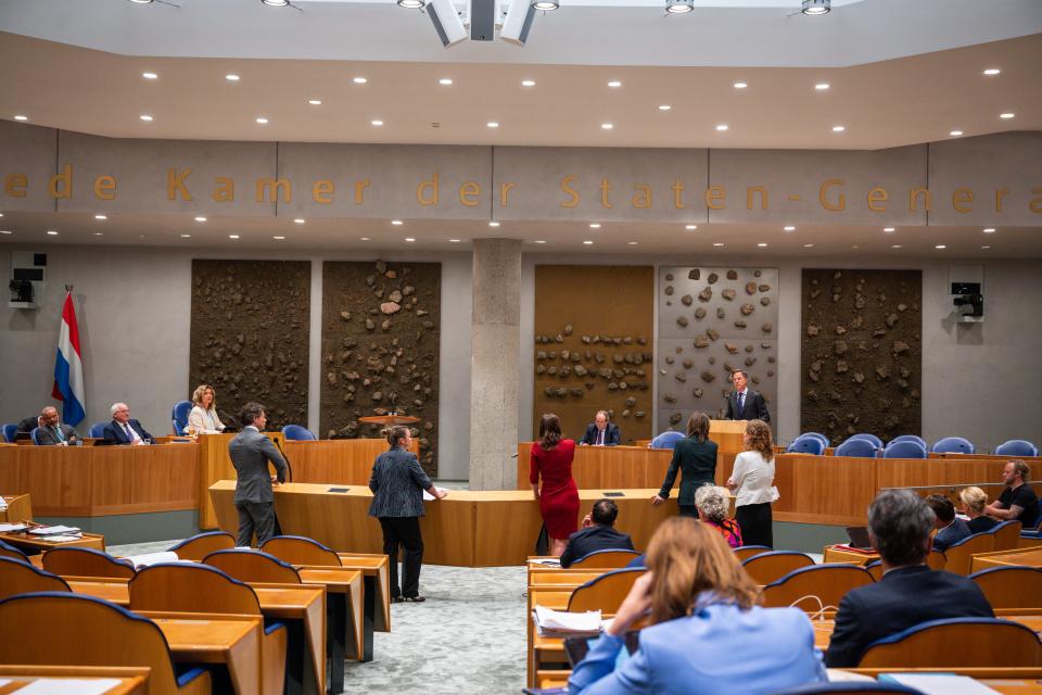 Minister-president Mark Rutte spreekt vanuit in vak K. Kamerleden staan voor hem bij de interruptiemicrofoons in de plenaire zaal.