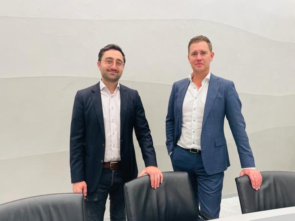 Twee Kamerleden poseren naast elkaar achter twee kantoorstoelen in een vergaderzaal van de Tweede Kamer.