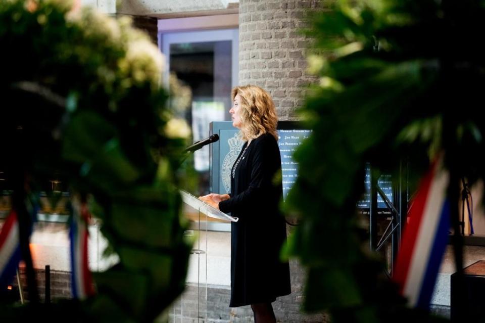Tussen twee kransen op de voorgrond staat Kamervoorzitter Vera Bergkamp achter een katheder terwijl zij haar speech uitspreekt. 
