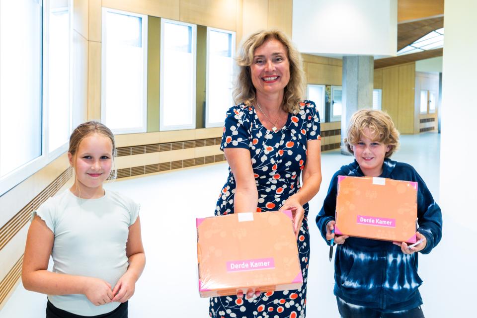 Kamervoorzitter tussen twee kinderen. Ze laten alledrie een leskoffer zien.