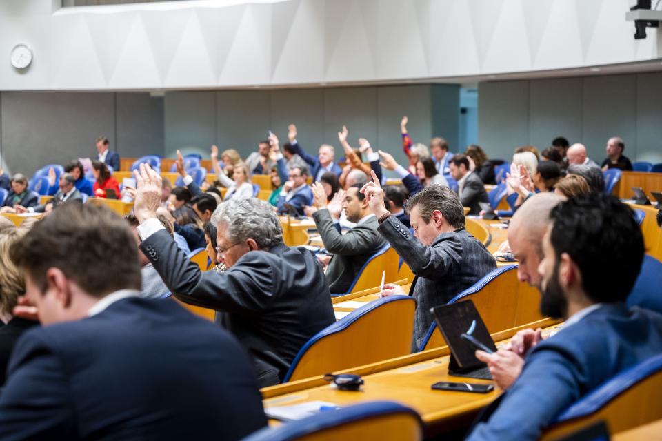Kamerleden zitten in de plenaire zaal en steken hun hand op tijdens de stemmingen.