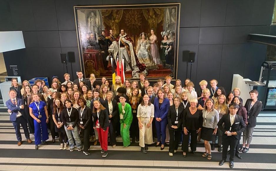 Grote groep jongeren uit de Benelux landen staat in een ruimte van het Ministerie van Buitenlandse Zaken voor een schilderij.