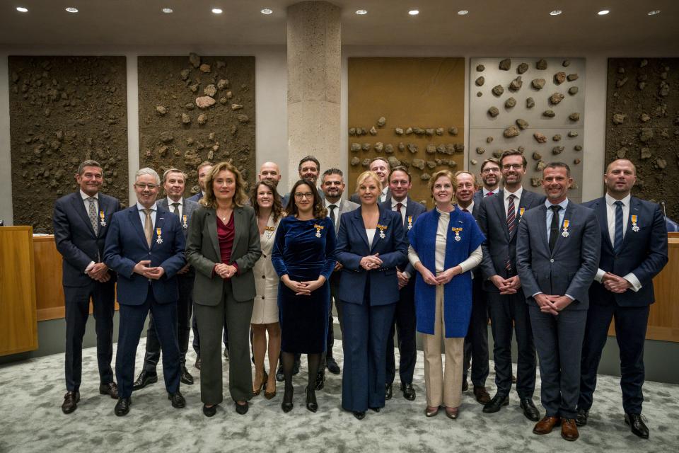 18 Kamerleden poseren met een koninklijke onderscheiding die zij opgespeld kregen van Kamervoorzitter Vera Bergkamp.