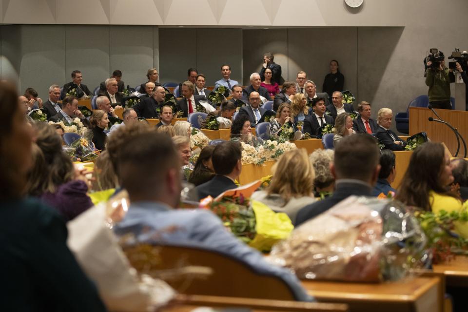 Kamerleden zitten in de plenaire zaal tijdens de beëdiging na de verkiezingen van 2023. Er liggen bloemen op de tafels voor ze.