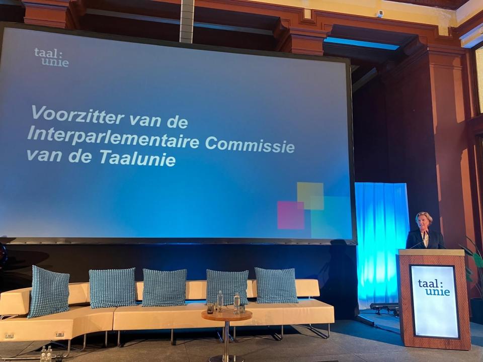 Mevrouw Geerdink (Eerste Kamerlid voor de VVD en delegatieleider) spreekt vanachter een katheder. Naast haar is een groot scherm te zien waarop een presentatie staat.