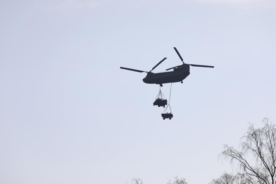 Helicopter in de lucht met daaronder goederen aan netten. 