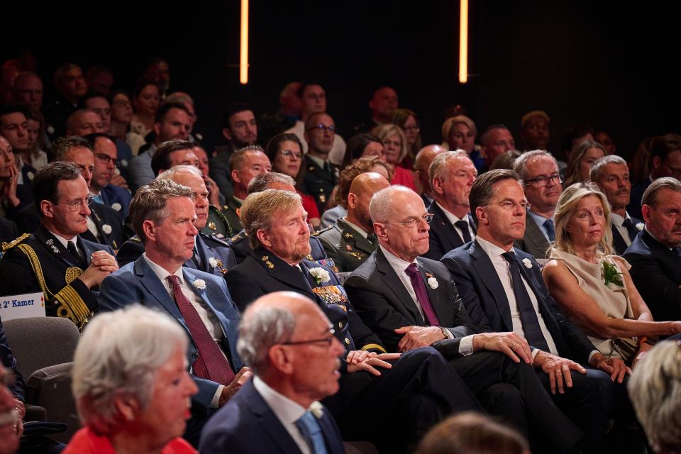 Personen zitten op stoelen in de Koninklijke Schouwburg.  Op de voorste rij van links naar rechts Tweede Kamervoorzitter Martin Bosma, Koning Willem-Alexander, Eerste Kamervoorzitter Jan Anthonie Bruijn, demissionair minister-president Mark Rutte en demissionair minister van Defensie Kajsa Ollongren.