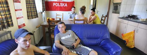 Poolse arbeidsmigranten zitten op een bank in een tijdelijke huiskamer.
