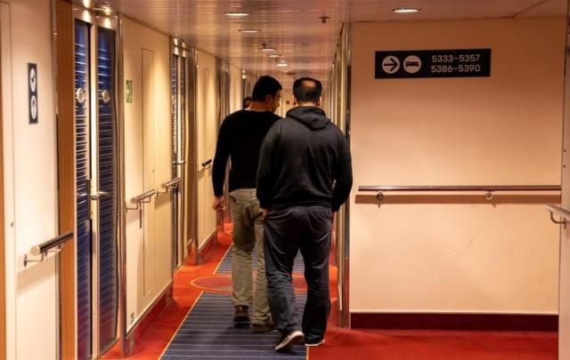2 mannelijke asielzoekers lopen in de gang van hun opvanglocatie.