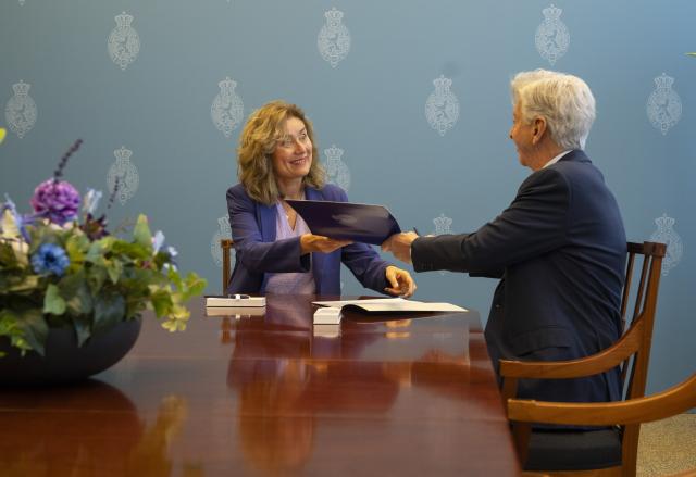 Kamervoorzitter Vera Bergkamp zit links aan een tafel in de Schrijfkamer en verkenner Ronald Plasterk rechts. Ze wisselen documenten uit.