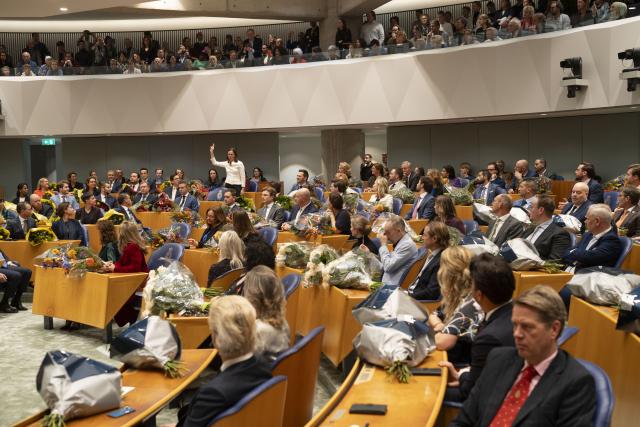 Overzicht van de plenaire zaal van de Tweede Kamer met alle Kamerleden op hun plek, achterin staat een Kamerlid op om de eed af te leggen.