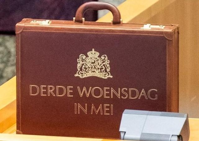 Koffertje met opschrift 'Derde woensdag in mei' staat rechtop op een tafel van de plenaire zaal in de Tweede Kamer.  